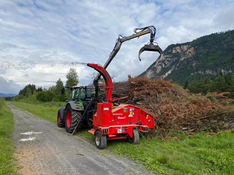 Traktor mit Eschlböck-Hacker beim Verarbeiten von Forstschnittgut an einem Weg vor Bergkulisse