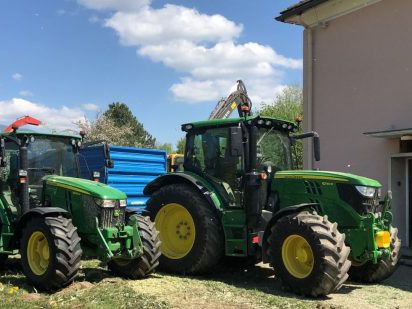 Zwei grüne Traktoren im Sommerdienst neben einem Gebäude, dahinter ein blauer Anhänger