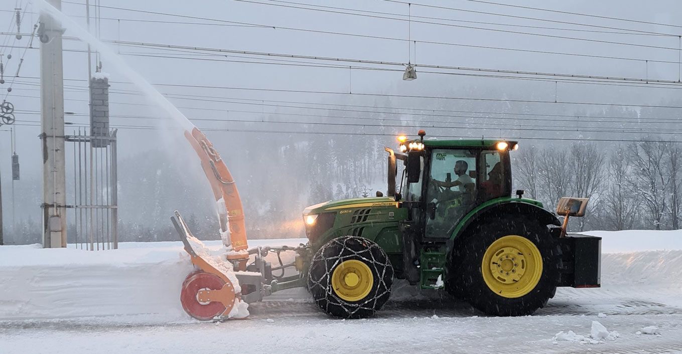 Traktor mit Schneefräse räumt eine verschneite Straße bei Schneefall
